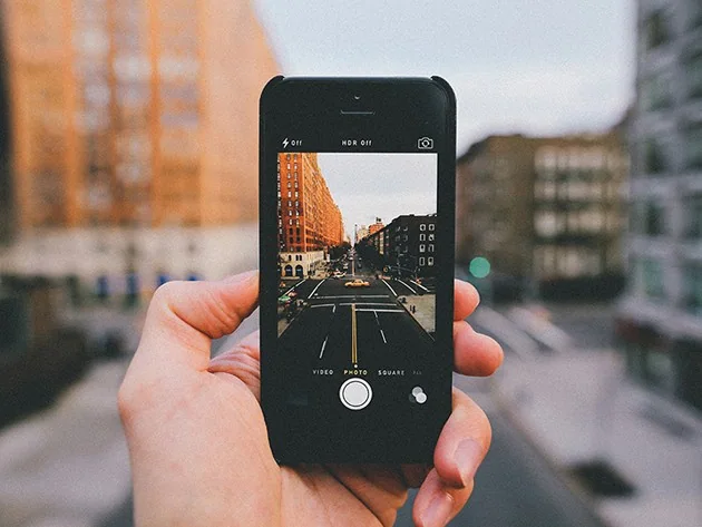 Person holding a smartphone to photograph a city street