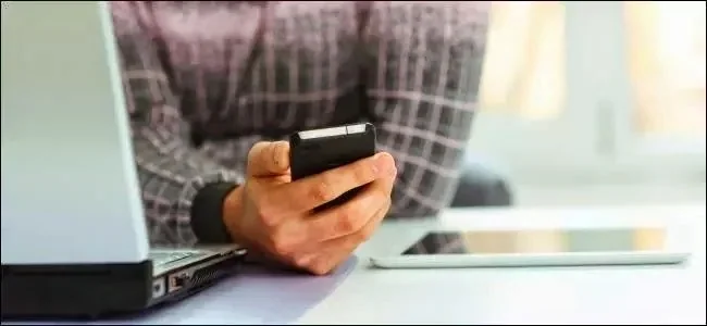 Person using a smartphone beside a laptop